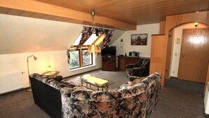 A living room with a sofa, a table, a lamp, a television, and a window with curtains. - Gemutliche Ferienwohnung in Altenberg (Altenberg)