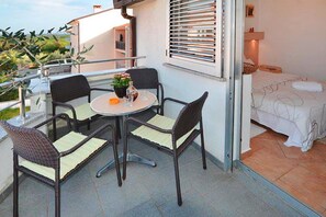 Een balkon met een tafel, stoelen, een bed en een raam met zonwering.