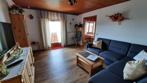 Een woonkamer met een houten plafond, een blauwe bank, een houten salontafel, een televisie en een houten kast.