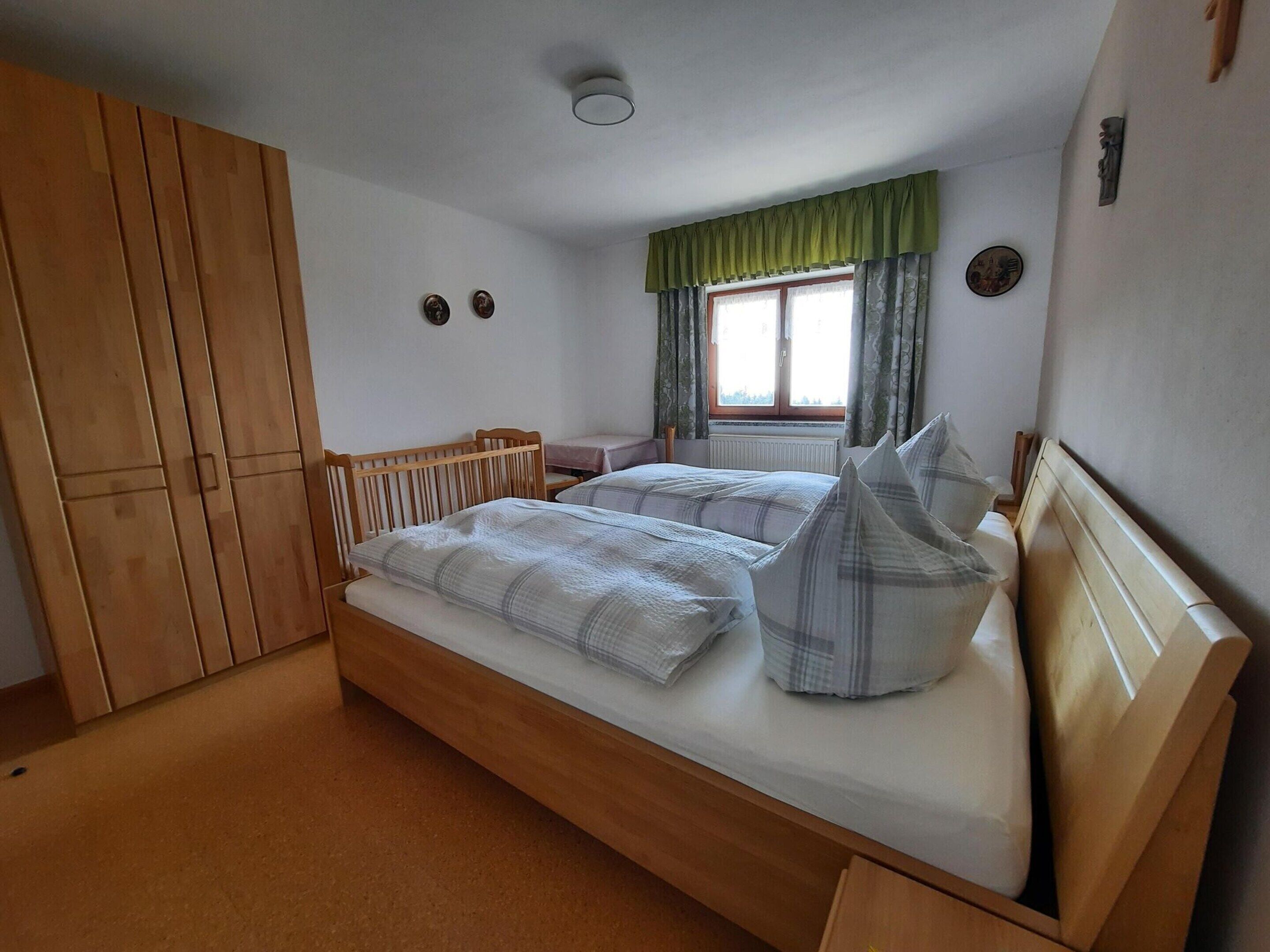 A bedroom with a wooden bed, a wardrobe, a window with curtains, and a radiator.