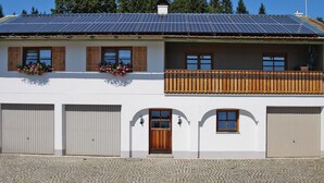 Een gebouw met twee verdiepingen, een witte gevel, houten balkon en zonnepanelen op het dak.