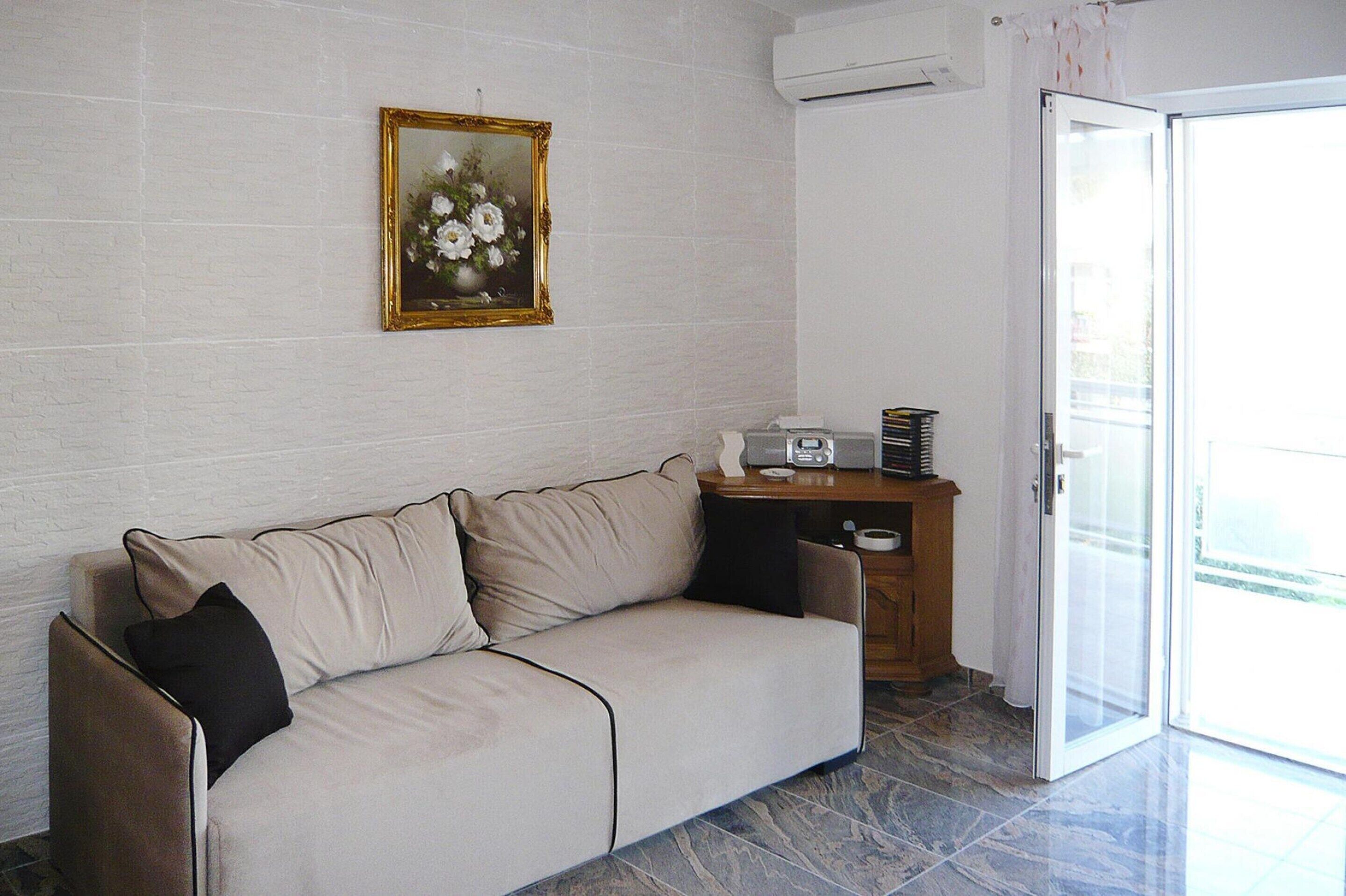 Una sala de estar con un sofá color beige, una mesita de madera, un cuadro en la pared y una puerta corrediza de vidrio que da a un área exterior.
