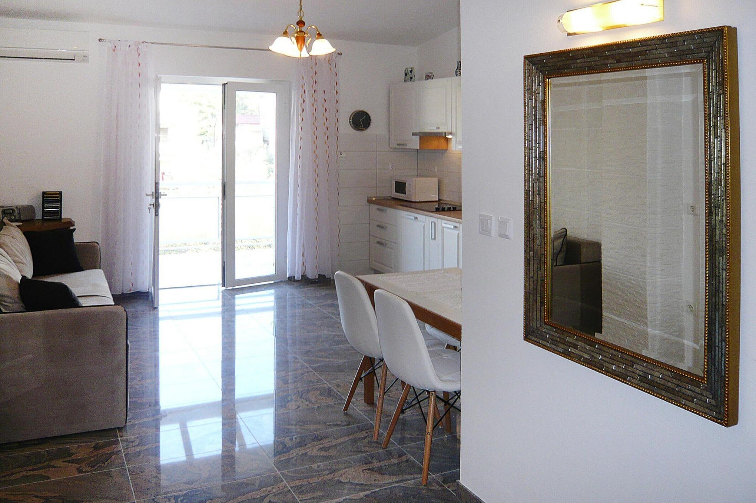 Una sala de estar con sofá, una mesa de comedor con sillas, un área de cocina con microondas y un espejo grande en la pared.