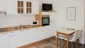 Une cuisine compacte avec des meubles blancs, un four à micro-ondes, un four traditionnel, un évier et une table à manger avec des chaises.