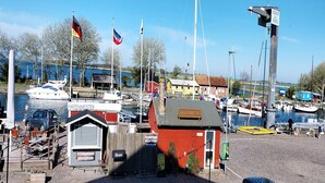 Een jachthaven met aangemeerde boten, een klein rood gebouw en een bord met 'Hafenmeister'.