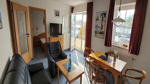 Een woonkamer met een bank, een eettafel met stoelen, een televisie en een raam met gordijnen.