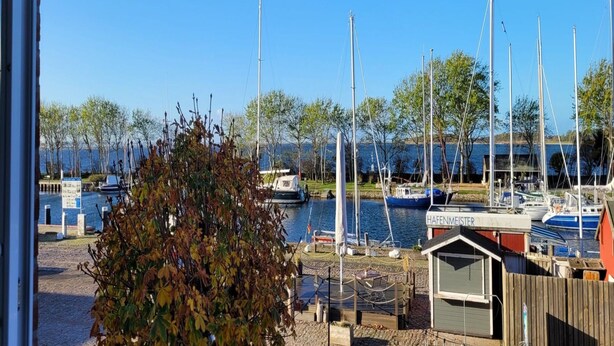 Een jachthaven met aangemeerde boten, een klein tuinhuisje met de tekst 'HAFENMEISTER' en uitzicht op het water.