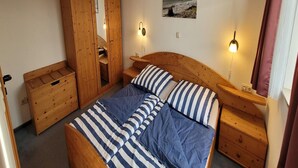 Een slaapkamer met een houten bed, gestreept beddengoed, een houten kledingkast, nachtkastjes en een aan de muur hangend schilderij.