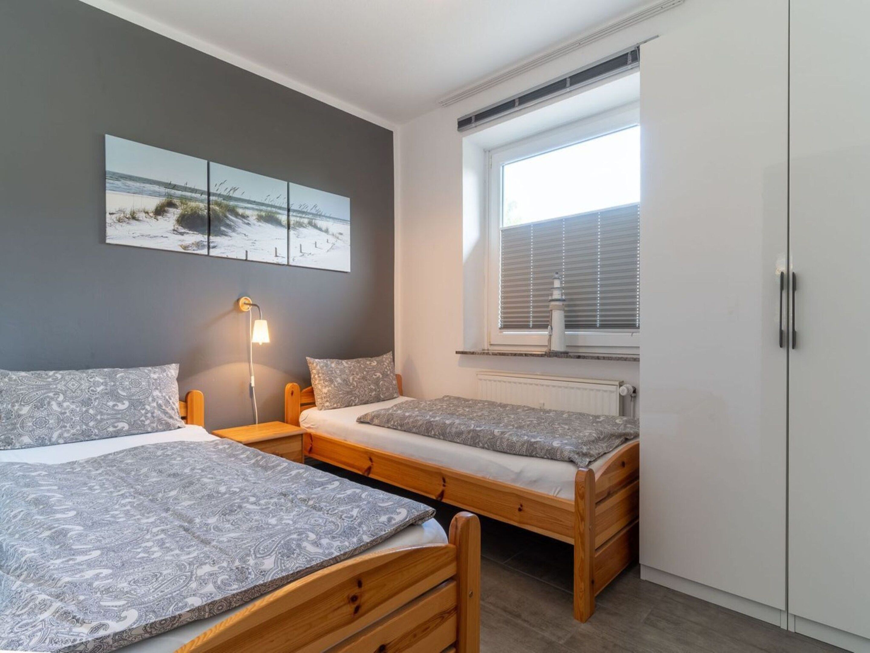 Un dormitorio con dos camas, una mesita de noche, una lámpara, un ventanal con persianas y un radiador.