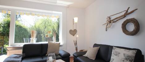 A living room with a black sofa, a wooden coffee table, and a window with a view of greenery.