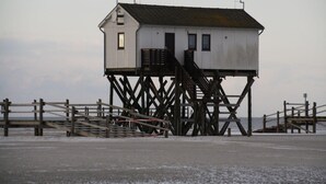 A white building with a staircase on stilts, a wooden fence, and a metal railing.
