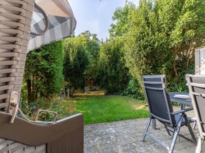 Un espace patio aménagé avec une table et des chaises, entouré d’un jardin luxuriant et d’arbres.