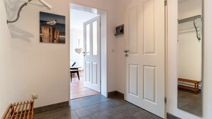 A hallway with a wooden bench, a white door, and a mirror reflecting a bench. - Ferienwohnung in St. Peter-ording (St. Peter-Ording)