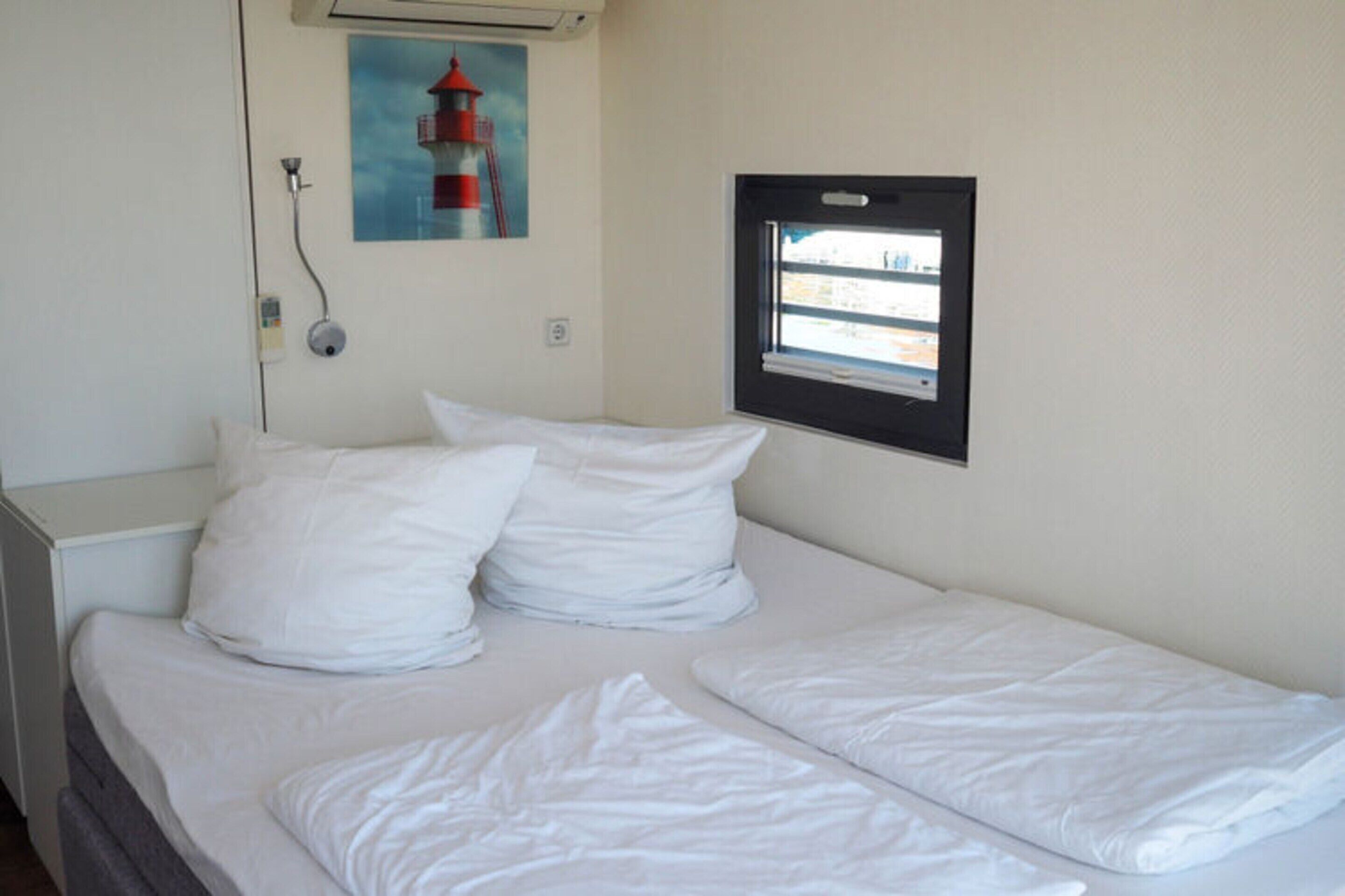 A single bed with white bedding, a window with a view, and a painting of a lighthouse on the wall.