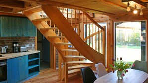 Una escalera de madera que lleva a un segundo piso, una cocina con armarios azules, una mesa de comedor con sillas y un jarrón de flores.