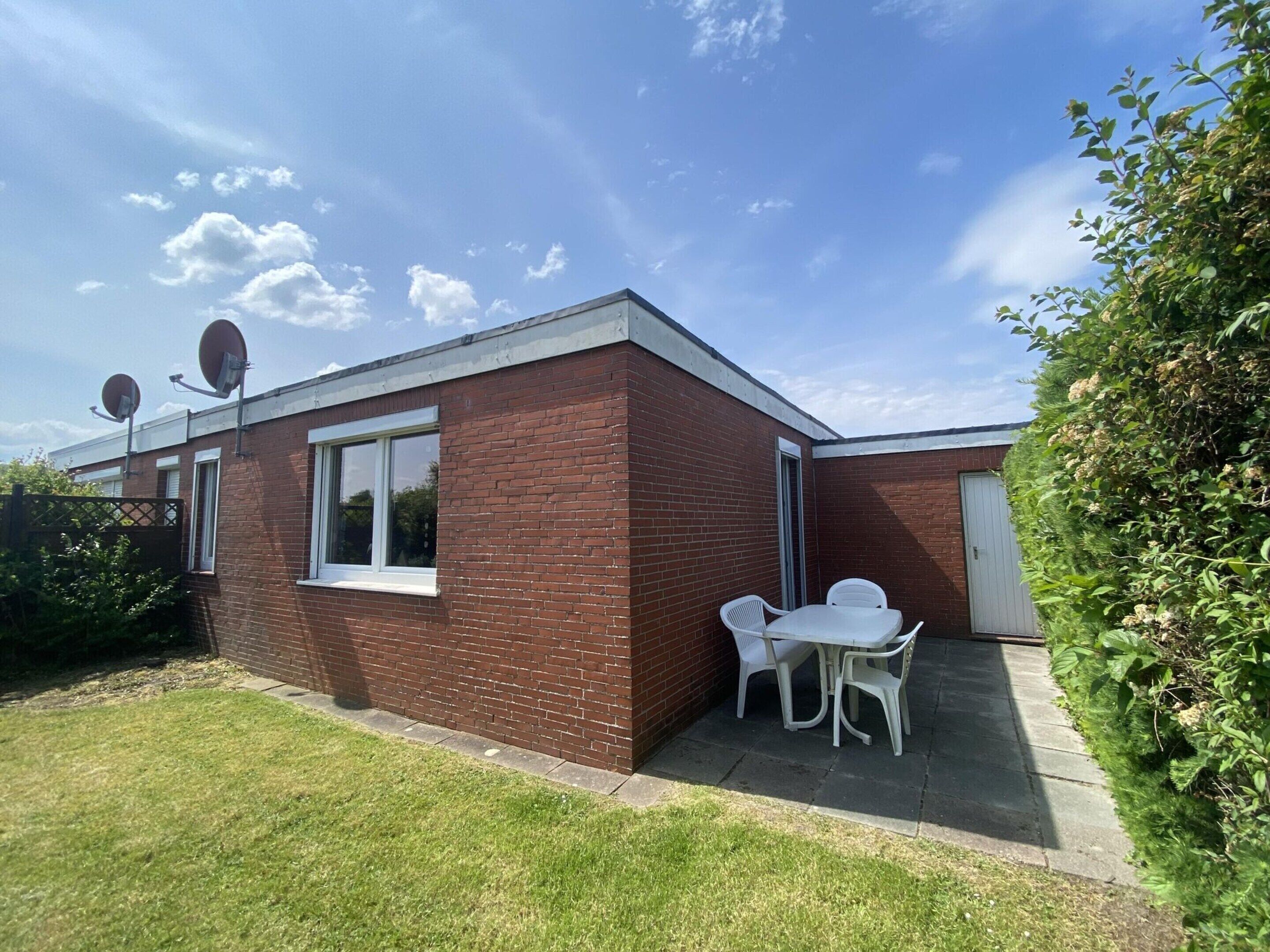 A single-story brick house with a small patio, a white door, and two satellite dishes.