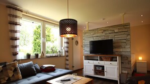 Ein Wohnzimmer mit Sofa, Couchtisch, Fernseher an einer Steinwand und Lampe.