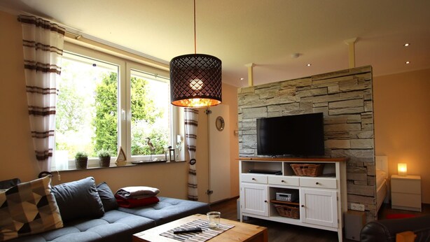 Ein Wohnzimmer mit Sofa, Couchtisch, Fernseher an einer Steinwand und Lampe.