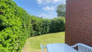 A patio with a white table and chairs, a brick wall, and a well-maintained lawn. - Bungalow in Dornumersiel (Dornum)