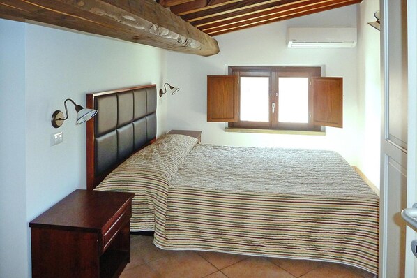 Une chambre à coucher comprenant un lit, des tables de chevet, une fenêtre avec des volets en bois et un appareil de climatisation.
