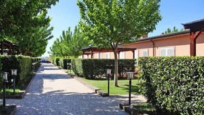 A paved pathway lined with neatly trimmed hedges and trees, leading to a row of buildings with a consistent architectural style. - Apartment in Vada With Garden Furniture (Rosignano Marittimo)