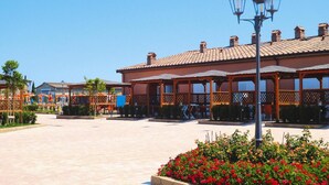 A spacious outdoor area with a building featuring a tiled roof and wooden latticework. - Apartment in Vada With Garden Furniture (Rosignano Marittimo)