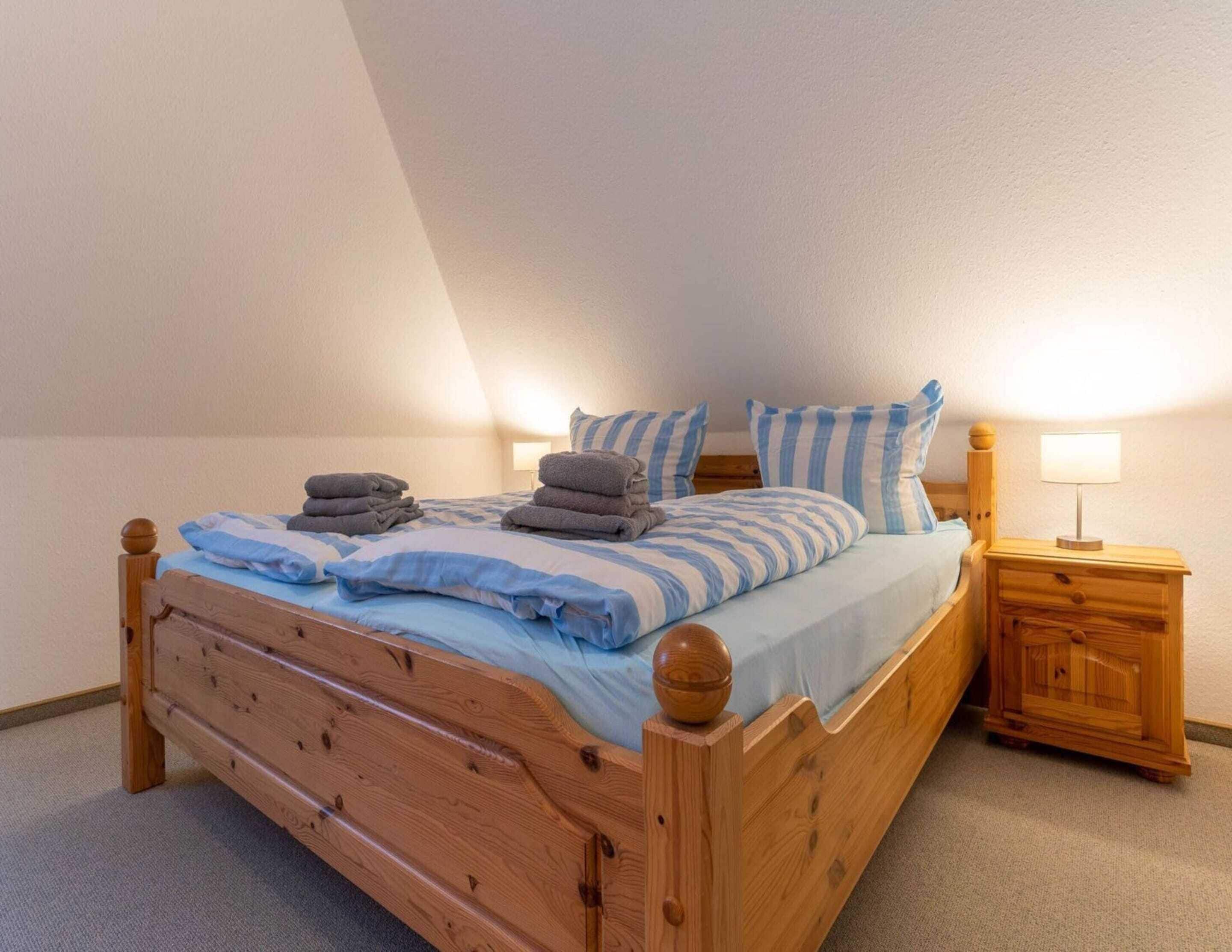 A wooden bed with blue and white striped bedding, a nightstand with a lamp, and a small wooden cabinet.