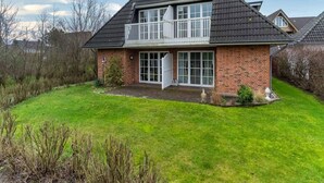 Una casa a due piani con un balcone, un garage e un prato curato.