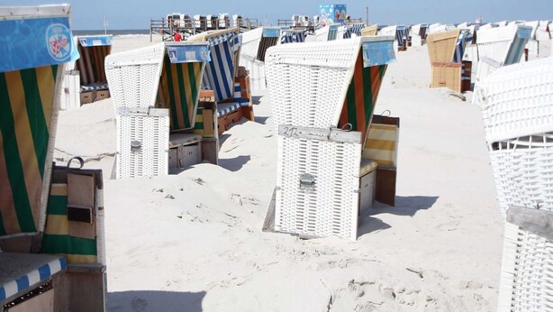 Capanne sulla spiaggia con tende a righe, disposte in file su una spiaggia sabbiosa.