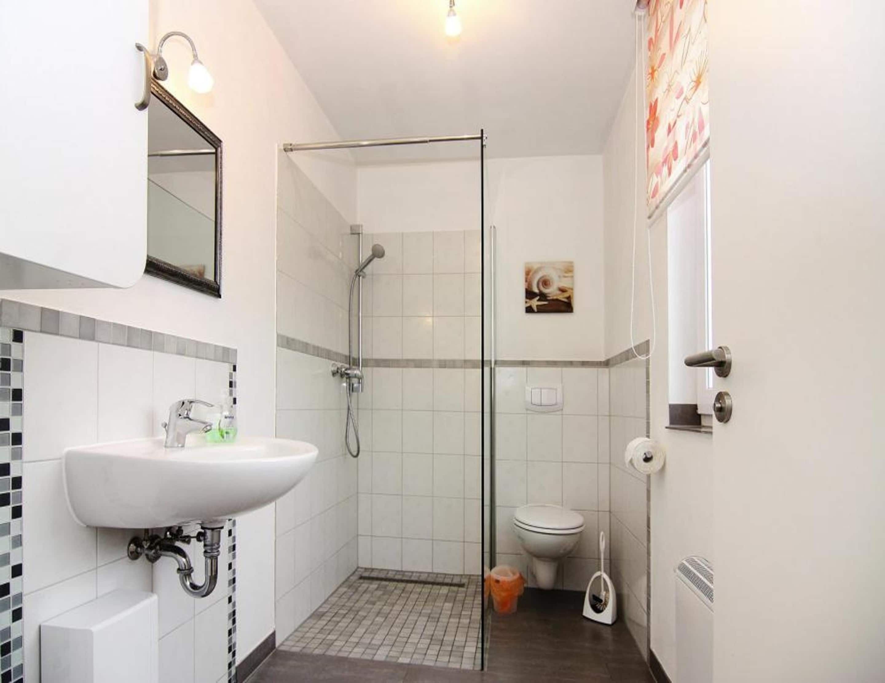 A small bathroom with a white sink, a glass shower enclosure, a toilet, and a mirror.