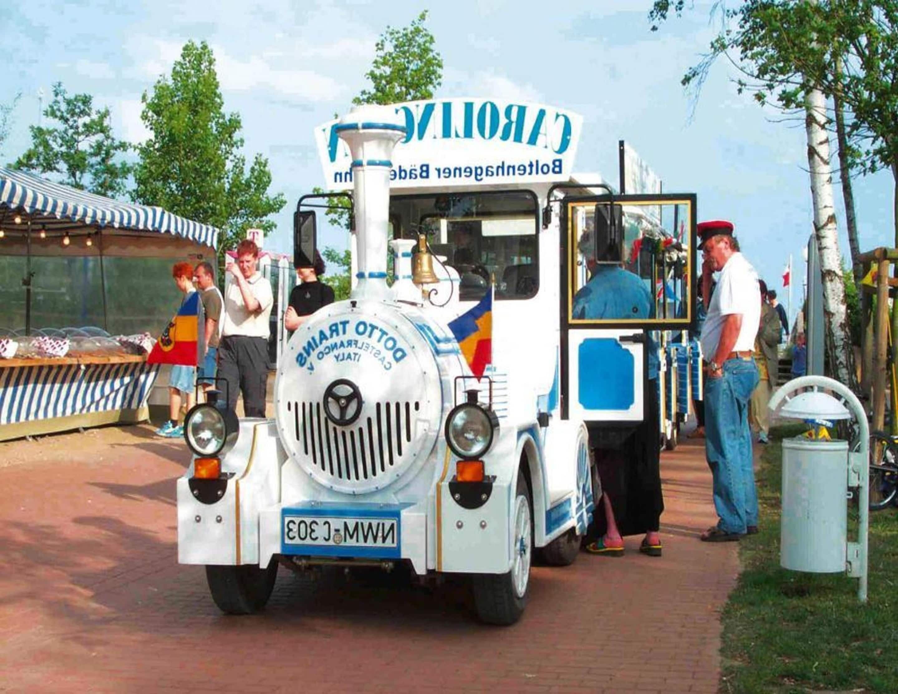 A vintage tram with a sign reading "CARTOON" and "BALTIC RIVER" parked on a paved area with people around it.