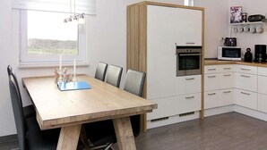 A modern kitchen with white cabinets, a wooden dining table, and a built-in oven.