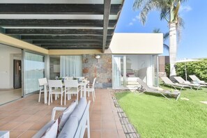 Een moderne buitenpatio met een eethoek, lounge stoelen en een stenen muur.