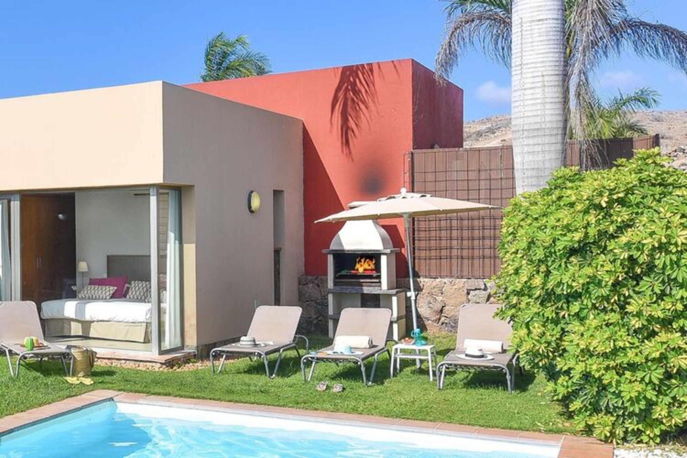 Ein moderner Außenbereich mit Pool, Liegestühlen, Grill und einem gläsernen Anbau mit Bett.