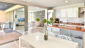 Een moderne keuken met witte kasten, een eethoek met tafel en stoelen, en een woonkamer met een bank en televisie.