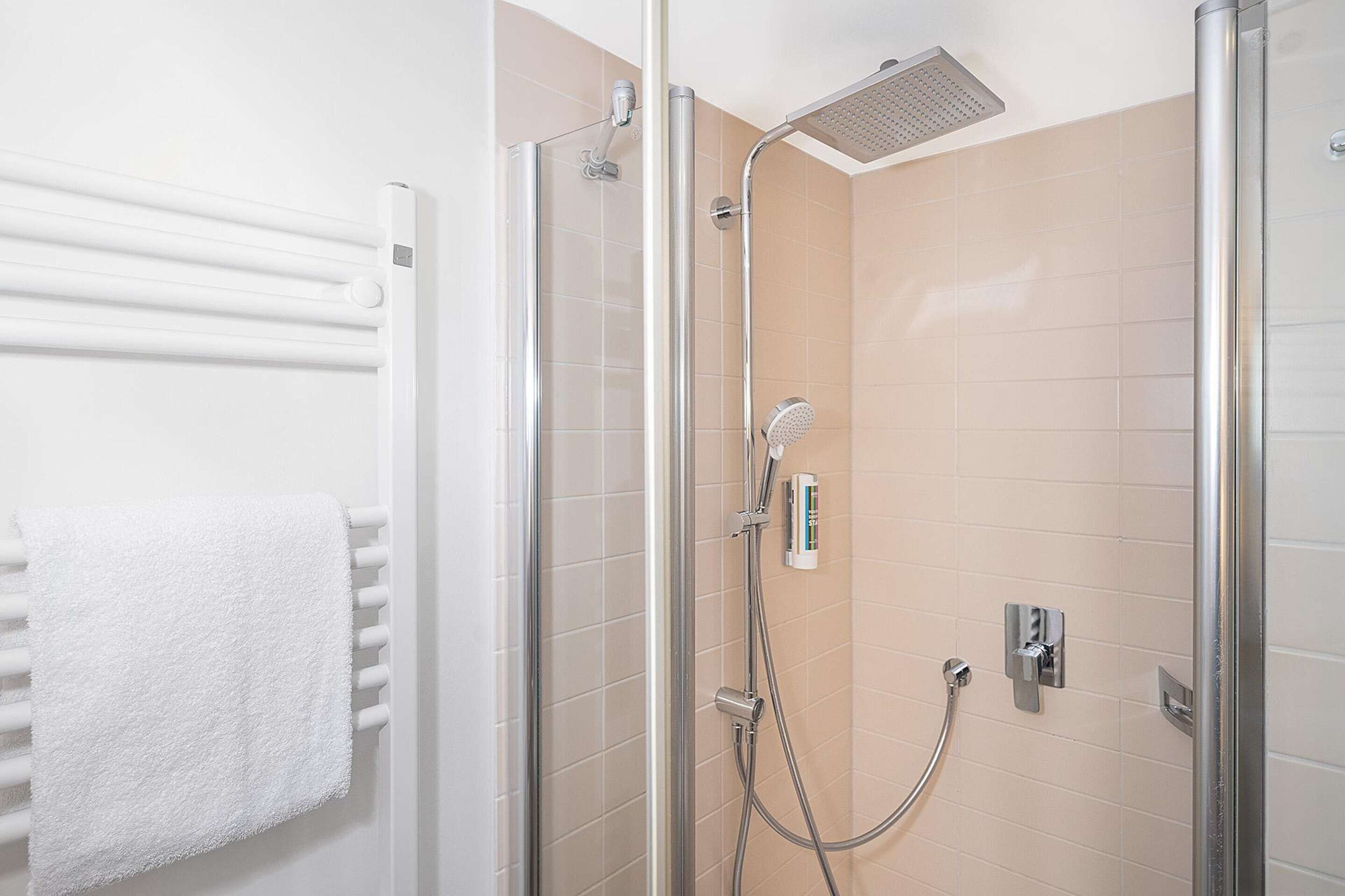 A glass-enclosed shower with a handheld showerhead and a wall-mounted control panel.