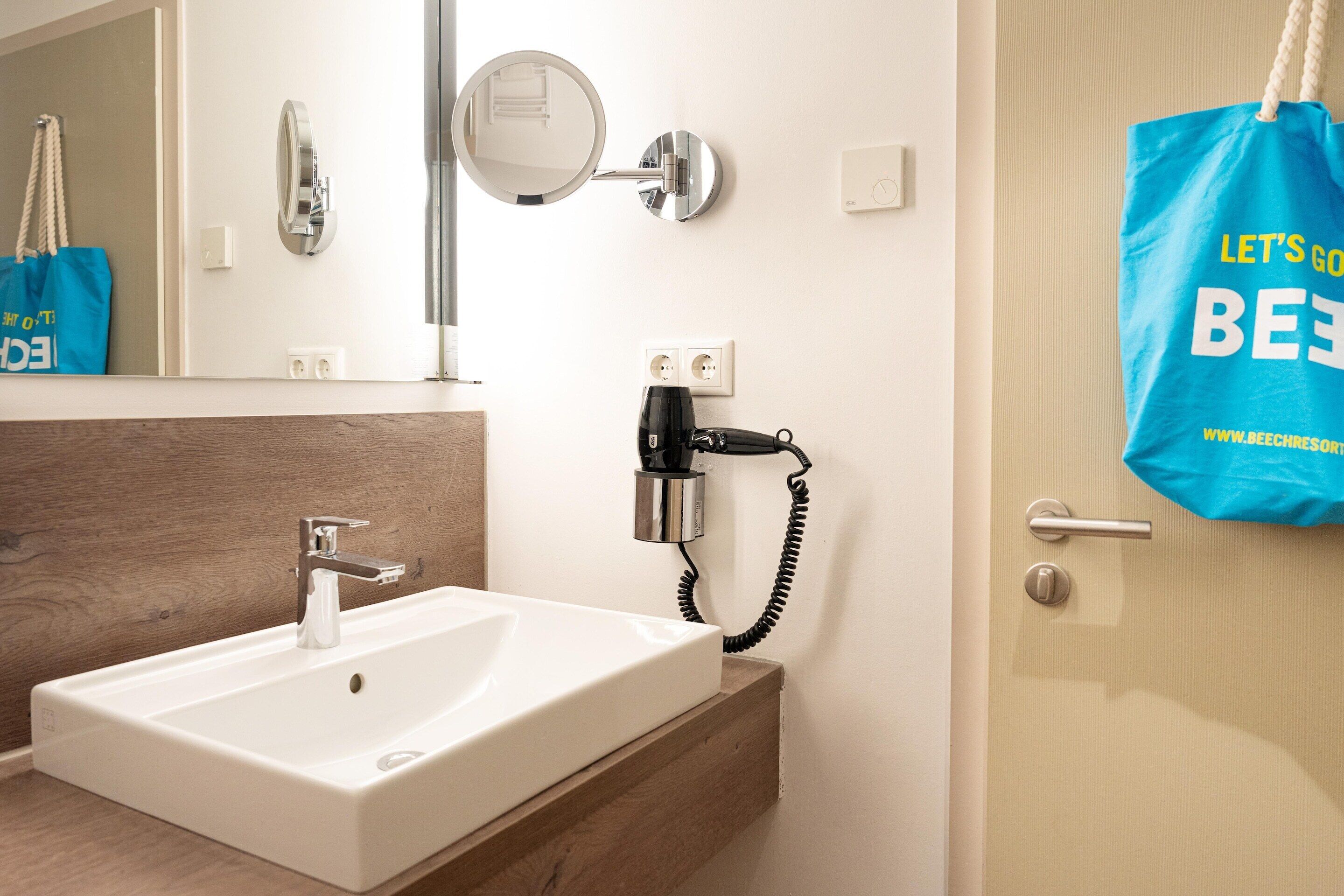 A bathroom with a white sink, a mirror, a hairdryer, and a blue tote bag hanging on the door.