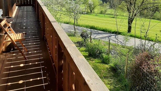 A wooden deck with a view of a green landscape and a river. - Ferienwohnung in Viechtach (Viechtach)