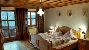 A wooden-framed bedroom with a bed, a nightstand, a chair, and a window with curtains. - Ferienwohnung in Viechtach (Viechtach)