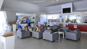 A modern lobby with grey sofas, a reception desk, and a counter with various items. - New Apartment in Baia Domzia Near the sea (Sessa Aurunca)