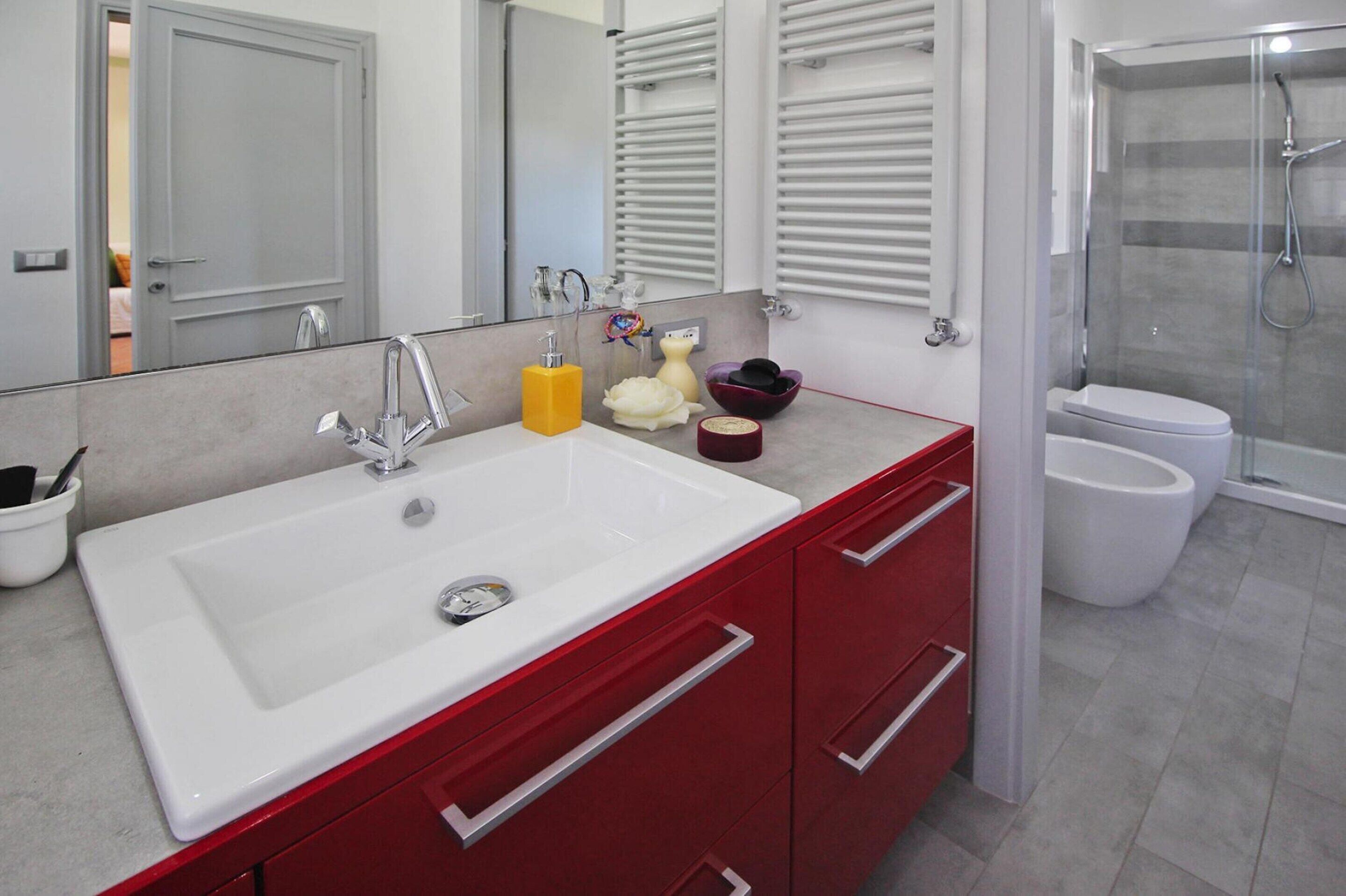 A modern bathroom with a white sink, red cabinets, and a glass-enclosed shower.