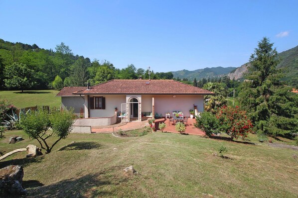 A single-story house with a tiled roof, a front porch with a bench, and a small garden area. - Villa in Camaiore With Panoramic Mountain Views (Camaiore)