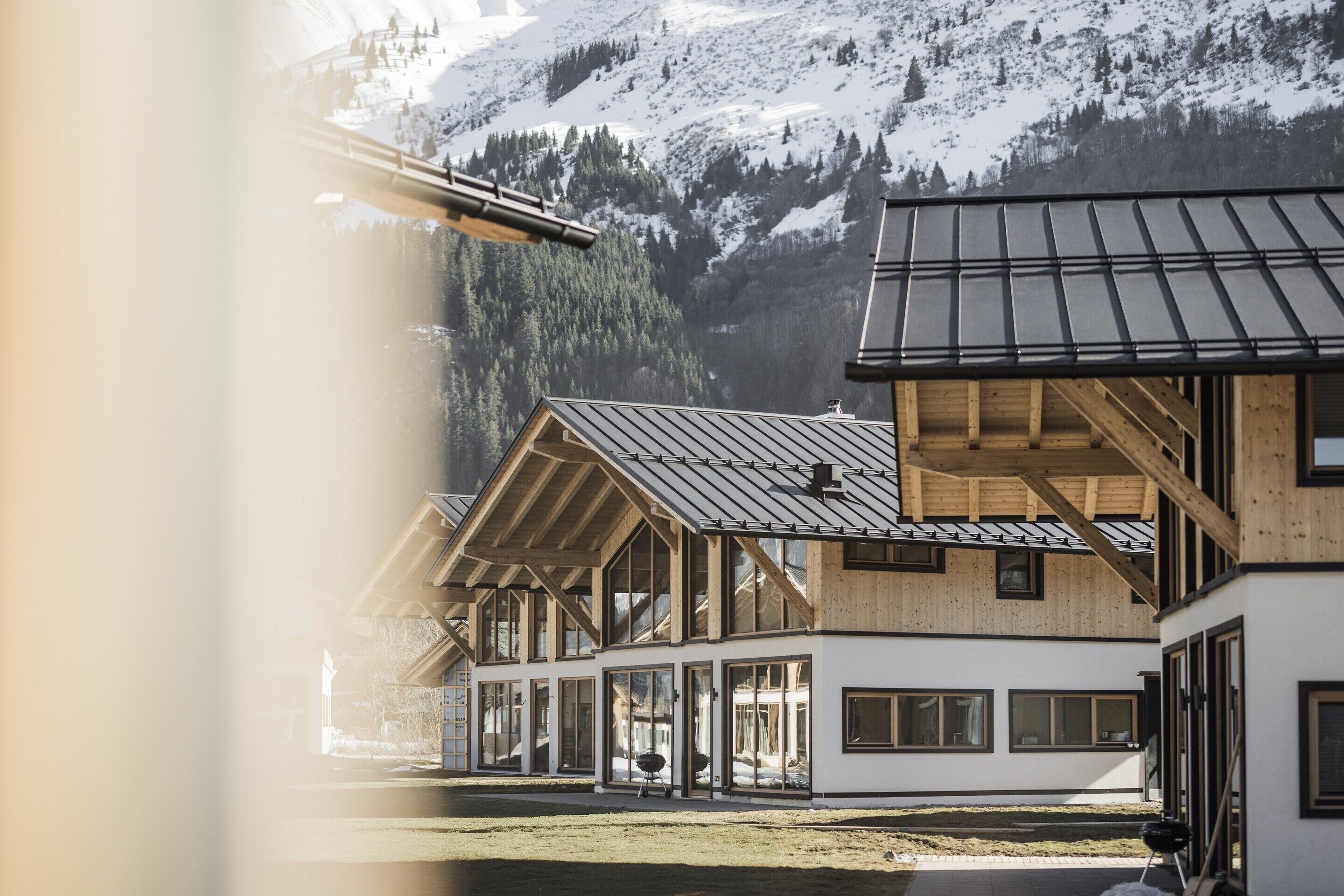 Eine moderne Chalet-Hütte mit großen Fenstern und Holzfassade vor einer verschneiten Berglandschaft.