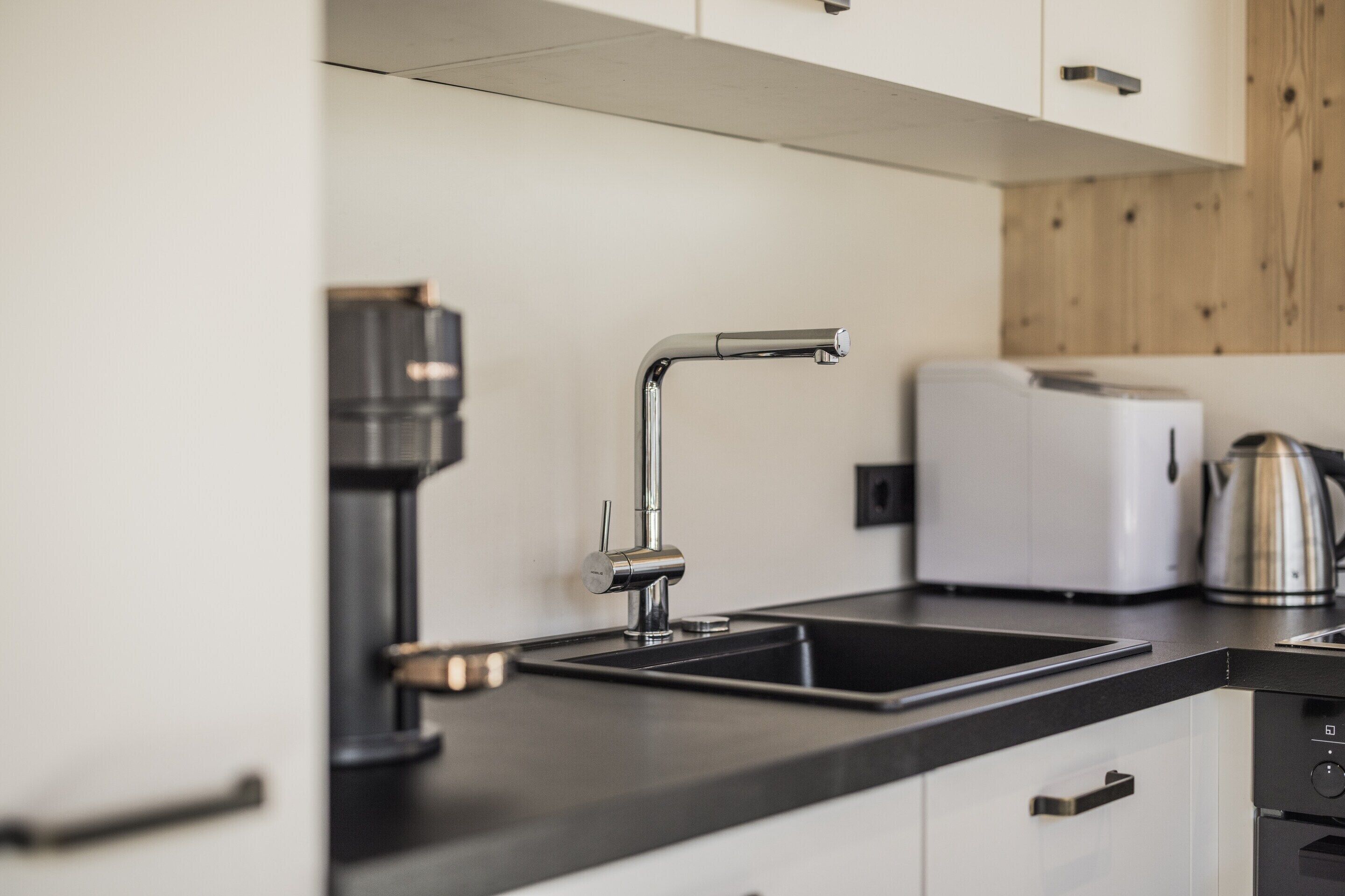 A modern kitchen with a black countertop, a stainless steel sink, a coffee maker, and a white toaster.