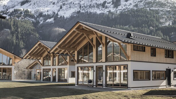 Un bâtiment moderne doté de grandes fenêtres et d’un toit en pente, entouré de montagnes enneigées.