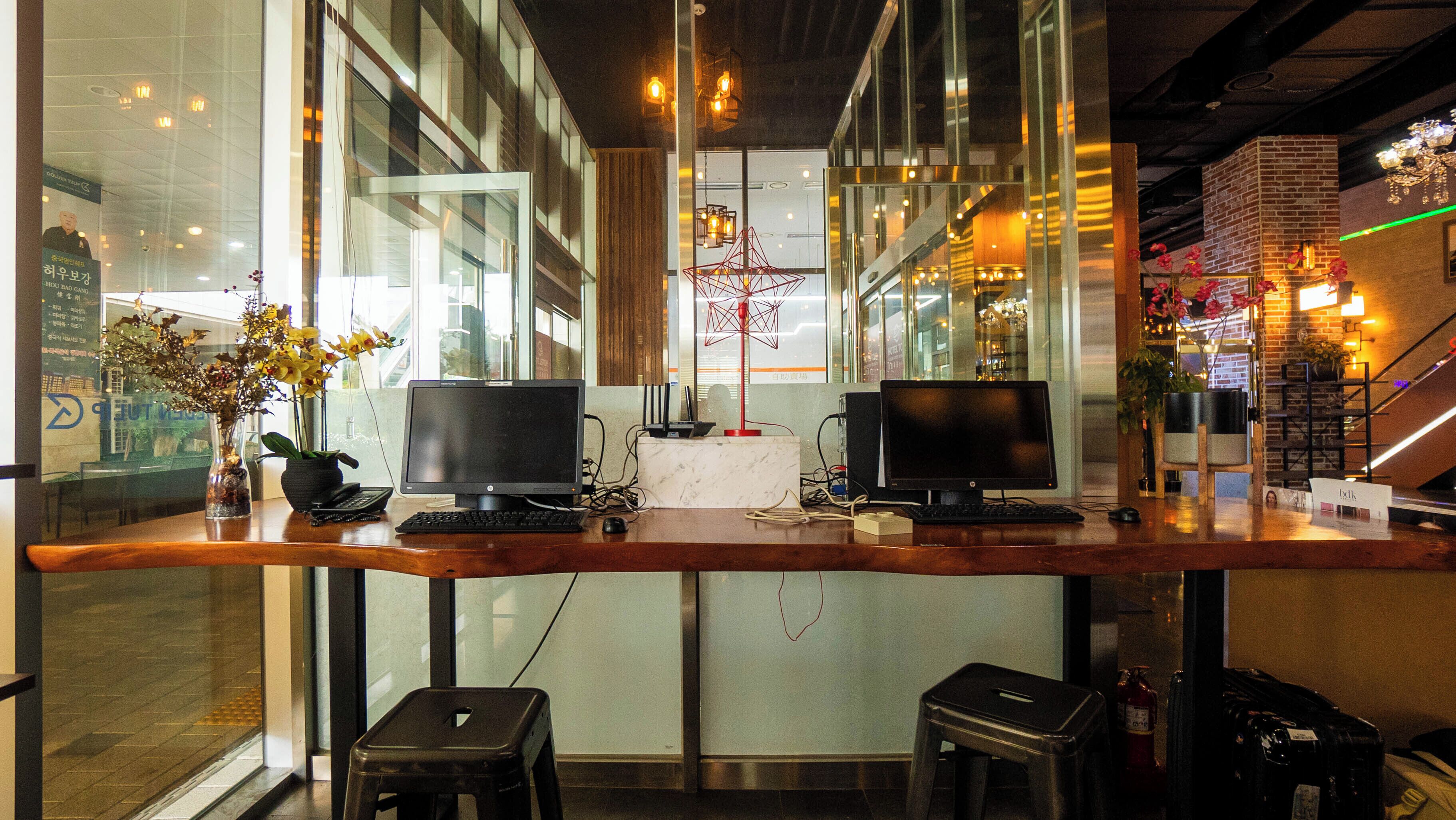 A workspace with two computer monitors, a vase with flowers, and a wooden desk.