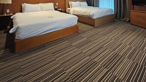 Habitació d'hotel amb dos llits, un televisor i una finestra gran amb cortines.