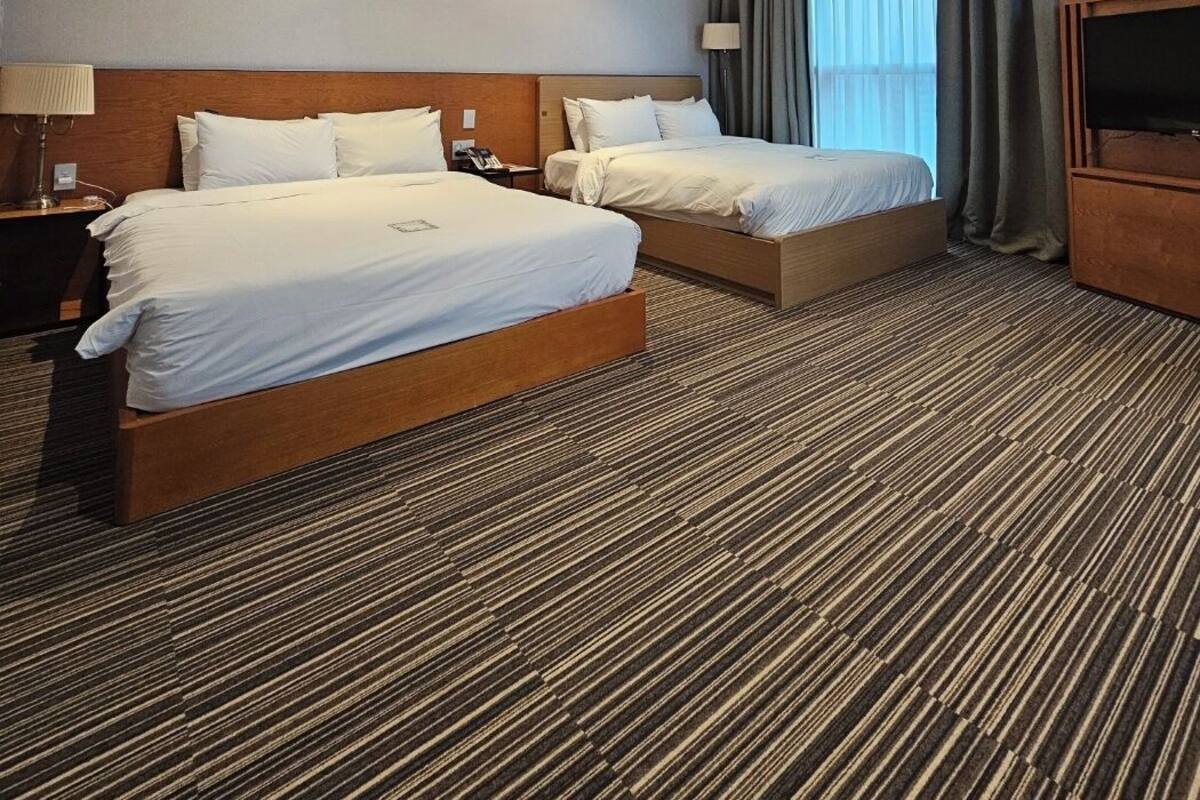 A hotel room with two beds, a TV, and a large window with curtains.