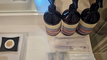 Una encimera de baño con productos para el cabello, un jabonera y paquetes de esponjas corporales.