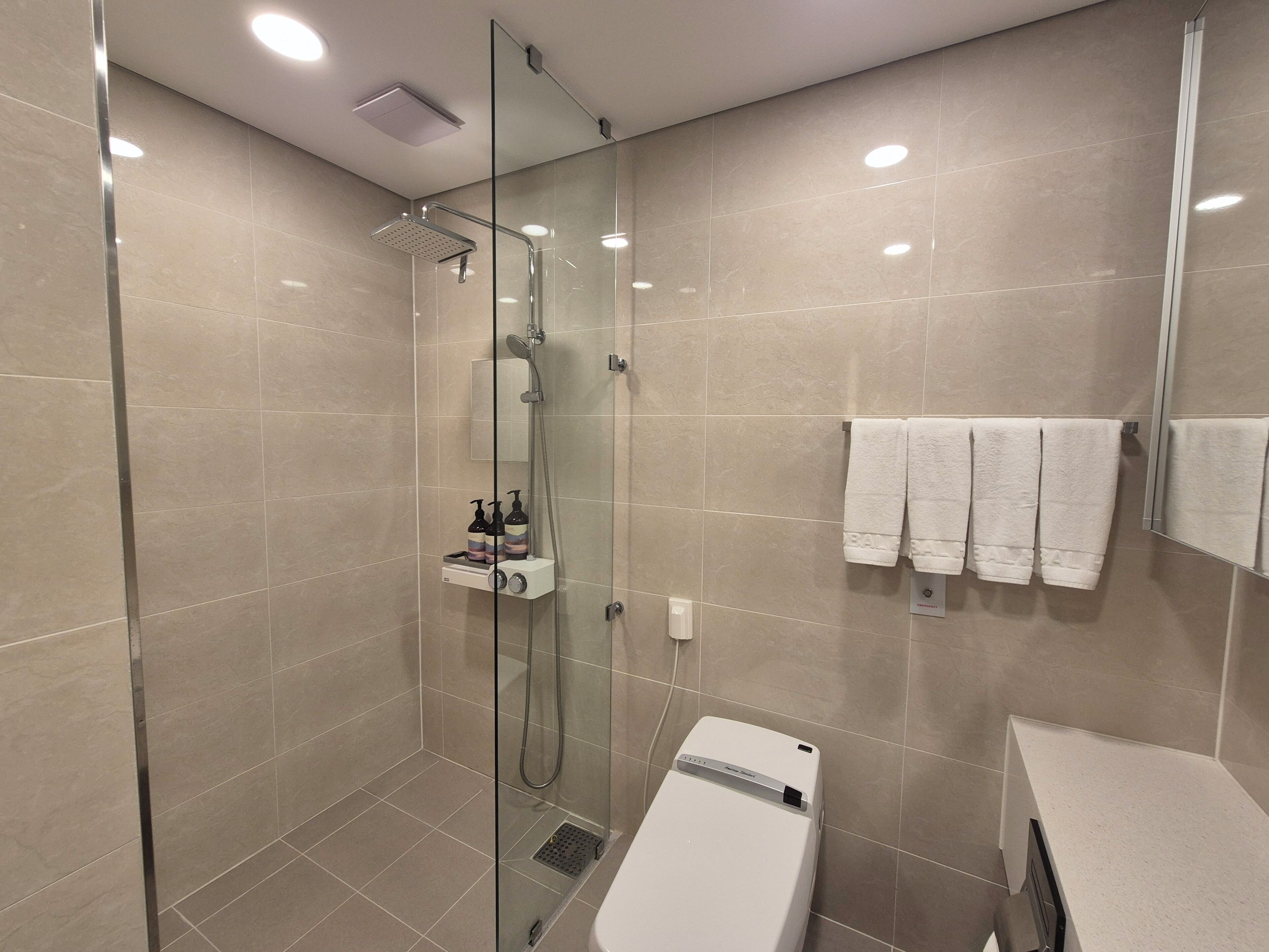 A modern bathroom with a glass-enclosed shower, a white toilet, and a towel rack with multiple towels.